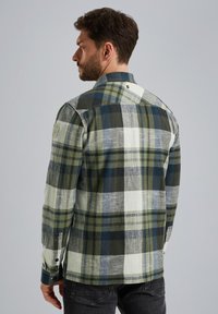 Chemise en flanelle à carreaux, verte, marine et blanche. Design à col avec fermeture à boutons, présentant des manches longues et un détail de poche latérale.