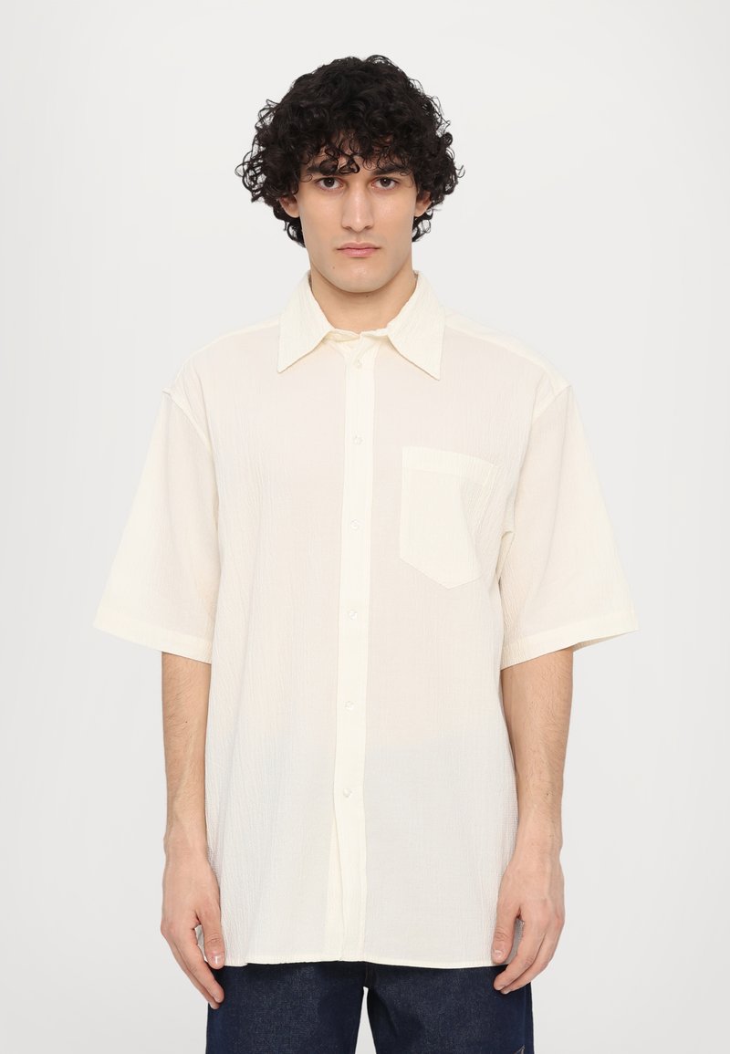 Chemise à manches courtes boutonnée en blanc cassé, en tissu texturé, avec une poche poitrine et un col classique. Coupe droite et coupe décontractée.