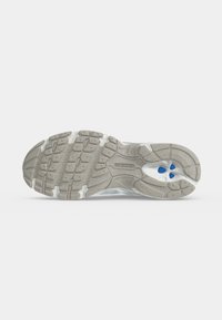 Σόλα από γκρι και λευκό παπούτσι New Balance με υφή πέλματος και τρεις μικρές μπλε ενθέσεις κοντά στην περιοχή της φτέρνας.