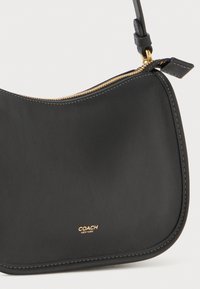 Black leather handbag with a curved shape, gold zipper, and gold logo "COACH NEW YORK." Smooth texture and minimalistic design accents.