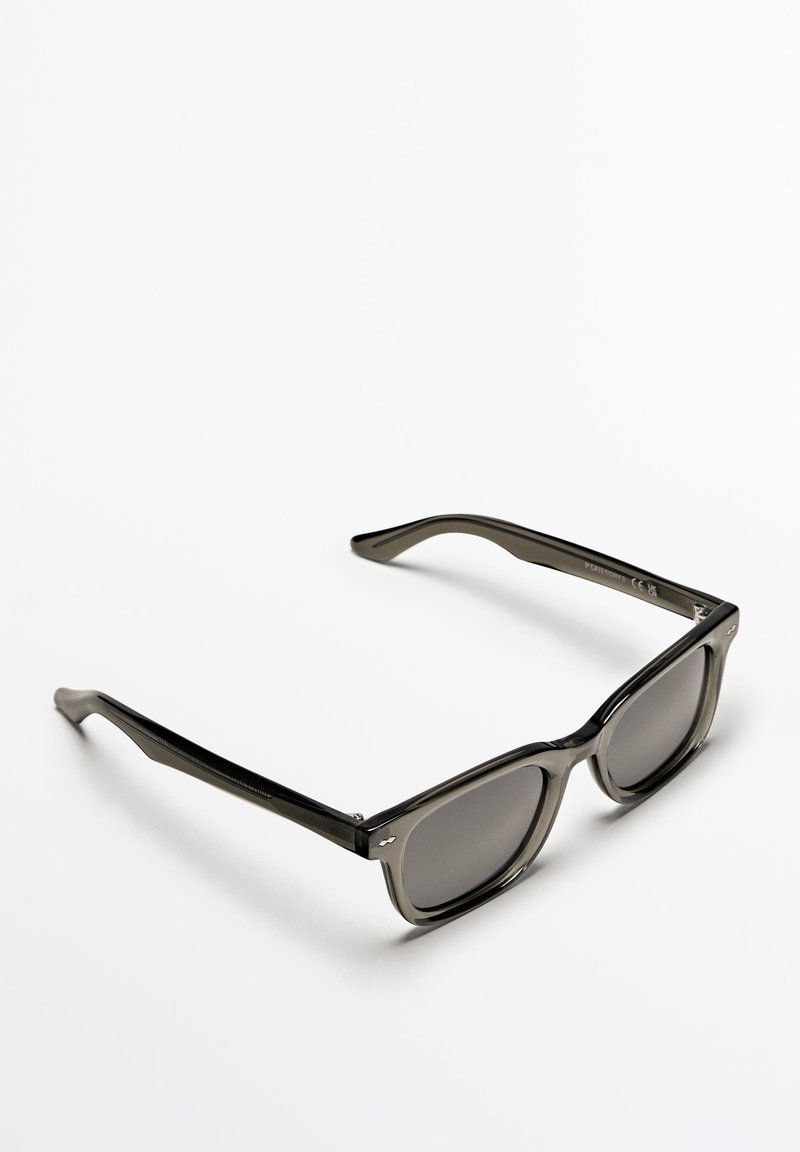 Grå plastsolglasögon med rektangulära bågar, tonade linser och subtil textur på sidorna. Bågarna är lätt böjda för en säker passform.