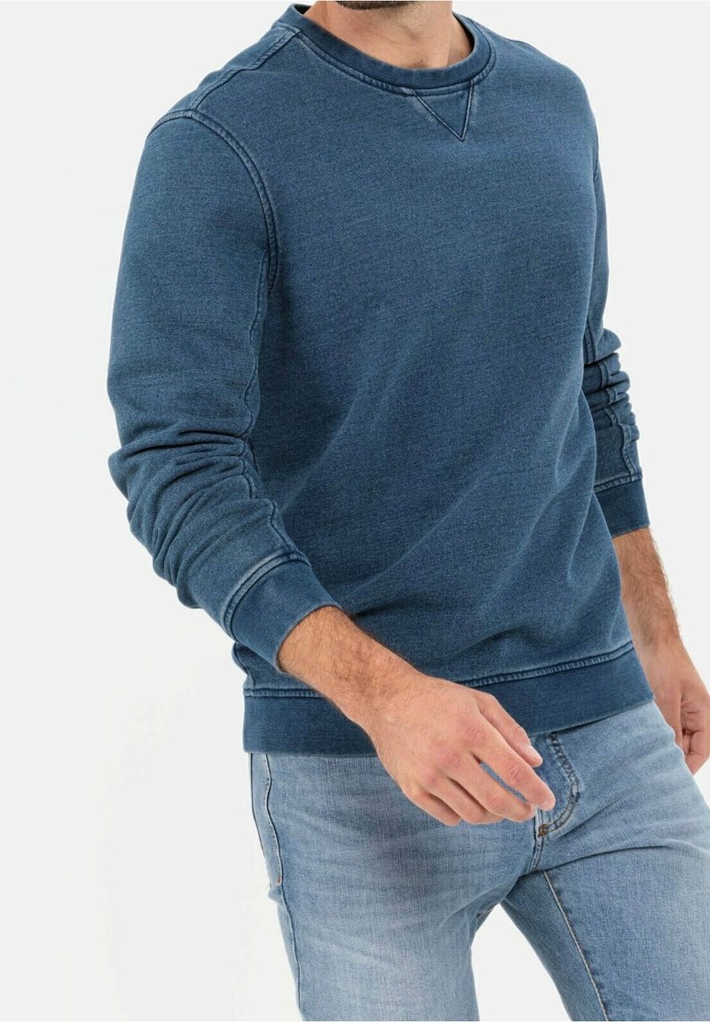 Felpa blu scuro a girocollo realizzata in materiale morbido. Presenta polsini e orlo a costine con dettagli di cucitura. Indossata con jeans azzurri.