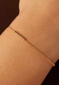Gouden armband met een delicate ketting, versierd met bolvormige accenten die gelijkmatig langs de lengte zijn verdeeld, en een strakke, minimalistische uitstraling hebben.