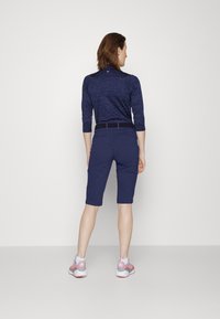 Marineblå shorts med slim fit, kneelengde, laget av stretchstoff. Har et vevd belte og baklommer. Kombinert med lys rosa fottøy.