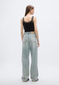 Juodas megztas trumpas megztinis su balta apdaila, derinamas su šviesiai mėlynais, aukštu liemeniu ir plačiomis kojomis džinsais, kuriuose yra kišenės detalė.