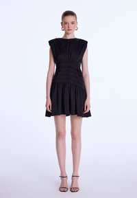 Robe noire avec épaules structurées, corsage froncé et jupe évasée. Fabriquée en tissu lisse, avec des accents plissés et un design minimaliste.