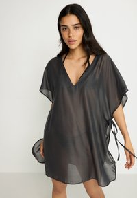 Crna prozirna kaftan haljina s V-izrezom, kratkim rukavima, bočnim vezicama i širokim krojem, izrađena od lagane, poluprozirne tkanine.