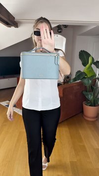 Lichtblauwe leren clutch met een ritssluiting, met een gladde textuur en een minimalistisch ontwerp. Merkennaam zichtbaar aan de voorkant.