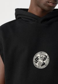 Close-up of black sleeveless hoodie with a white circular logo showing two boxers and text "Hugo Boxing Academy 1993 Athletics."