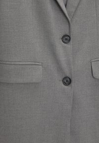 Szara marynarka wykonana z teksturowanej tkaniny, posiadająca dwie przednie kieszenie, wycięty kołnierz i czarne guziki z czterema dziurkami.