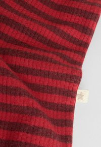 Röd och mörkbrun randig tyg, med en ribbad textur och en liten krämfärgad tagg på kanten. Materialet verkar mjukt.