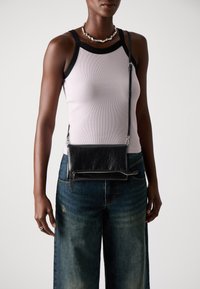 Borsa a tracolla nera in pelle con superficie texturizzata, dettagli in metallo argentato, e tracolla regolabile, abbinata a una maglietta aderente e jeans a gamba larga.