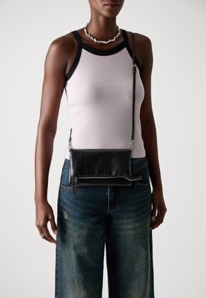 Sac en bandoulière noir en cuir avec une surface texturée, détail de zip argenté et bandoulière ajustable, associé à un haut ajusté et un jean ample.
