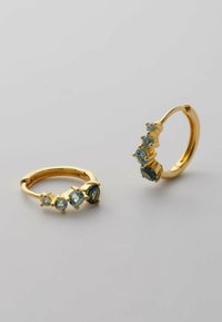 Guld hoopsörhängen med tre blå ädelstenar, med en slät yta och rundad design. Ädelstenarna varierar i storlek och är säkert infattade.