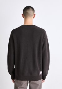 Brown knitted sweater with a textured surface, round neckline, and long sleeves; features a label near the hem on the back.