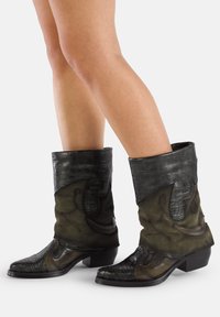 Buty w stylu zachodnim wykonane z mieszanych tekstur; ciemnozielony zamsz z tłoczonymi akcentami z czarnej skóry, spiczasty czubek i niski obcas.