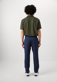 Green patterned short-sleeve shirt with a collar, paired with navy trousers. The outfit is completed with white athletic shoes.