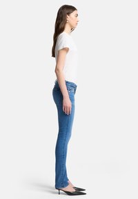 Skinny-fit blauwe jeans in denim met een middelhoge taille, gecombineerd met een witte t-shirt met korte mouwen en zwarte puntige hakken.