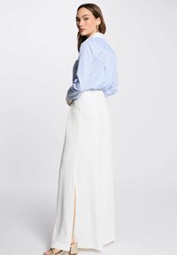 Camicia button-up a righe blu con colletto bianco, abbinata a pantaloni larghi bianchi con fessure laterali, che evidenziano una silhouette elegante.