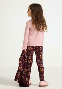 Lyserød ribbet langærmet top, blomstrede leggings i mørk burgundy og lyserøde sko. Barnet holder en matchende jakke med blomsterdesign.