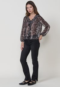 Blusa trasparente con stampa a serpente, colletto arricciato e maniche lunghe. Abbinata a jeans neri con un motivo sottile e spacchi all'orlo.