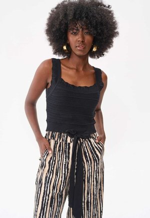 Zwarte gebreide tanktop met gerafelde randen, gecombineerd met hooge taille beige broek met zwarte verticale strepen en een gestrikt tailleband.