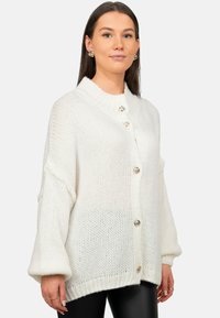 Witte, oversized gebreide cardigan met een geribde kraag, knoopsluiting, oversized mouwen en zilveren knoopaccenten. Textuur en lichtgewicht ontwerp.