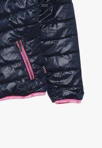 Námořnická puffer bunda s prošívaným designem, lesklou texturou, bočním růžovým zipem a růžovým akcentním páskem na lemu s textem. Měkká a mírně polstrovaná.