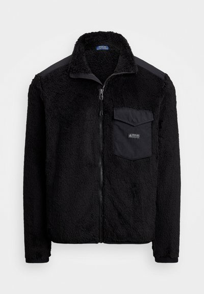 Svart fleece jakke med glidelås foran, høy krage og brystlomme. Teksturert stoff med en glatt skulderpanel som aksent.