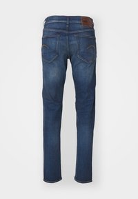 Denim jeans in dark blue with a smooth finish, featuring a branded brown leather patch and two back pockets with contrasting stitching.