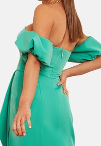 Dopasowana sukienka na ramiączkach w jasnym odcieniu turkusowym, z bufkami, z zamkiem błyskawicznym na plecach i gładką fakturą.