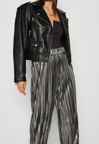Černá kožená zkrácená motorkářská bunda se stříbrnými zipy a knoflíky, v kombinaci s lesklými plisé metalickými stříbrnými kalhotami širokého střihu.