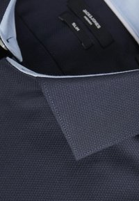 Paita tummansinisellä kauluksella, jossa on teksturoitu kangas, slim fit -leikkaus ja vaaleansininen sisäkaulus, joka erottuu. Etiketit näkyvät kauluksen sisällä.