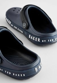 Marineblå gummitræsko med ventilationshuller, tekstureret indersål og hvid tekst "BAKER by TED BAKER" på siden. Justerbar hælrem.