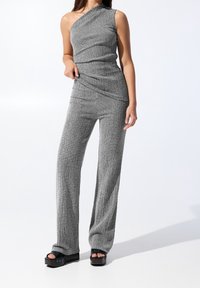 Szara, teksturowana, dziana bluzka na jedno ramię, zestawiona z dopasowanymi szerokimi spodniami. Czarne sandały na platformie z dekoracyjnymi detalami.