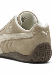 Beige mockasin-sneakers med texturerade sidostråk, vita detaljer och gummisula. Har en vadderad krage för extra komfort.