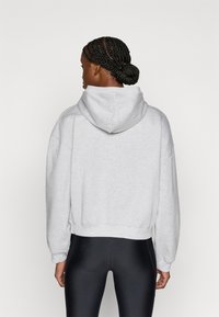 Γκρι φούτερ με κουκούλα και κομψό, κοντό σχέδιο, με φαρδιά μανίκια και απαλή υφή. Η όψη από πίσω δείχνει την κουκούλα και το ελαστικό τελείωμα.