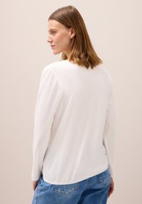 Weißes Langarmshirt mit Rundhalsausschnitt, aus weichem Stoff und lockerer Passform, kombiniert mit hellblauen Jeans.
