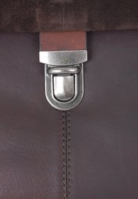 Rjava usnjena torba z teksturirano površino, s srebrnim kovinskim zapiranjem in gladkim rjavim trakom. Vidno šivanje ob šivu.