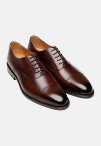Braune Lederschuhe mit glatter Oberfläche, spitzen Zehen und einem Schnürsystem mit sechs Ösen. Merkmale sind eine kontrastierende dunkle Zehenkappe und detaillierte Nähte.