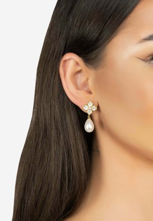 Gold drop earrings feature a flower design with clear stones, complemented by a large pearl hanging from the base.