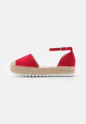 Rote Wildleder-Espadrille mit einer geflochtenen Jute-Plateau-Sohle, verstellbarem Knöchelriemen und einer weißen Gummisohle mit gezacktem Rand.