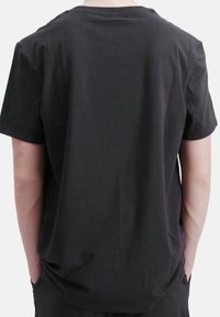 Camiseta de algodón negra con mangas cortas, cuello redondo y un corte holgado. La parte de atrás es lisa, mostrando la suavidad de la textura de la tela.