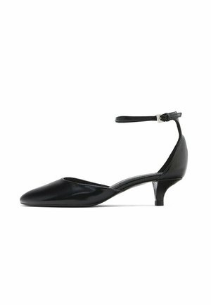 Chaussure en cuir verni noir avec un bout pointu, un petit talon compensé et une sangle ajustable à la cheville pour un maintien sécurisé. Texture lisse et design élégant.