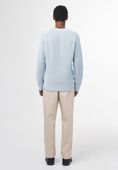Maglioncino azzurro chiaro a maglia con texture a coste, scollo rotondo e maniche lunghe, abbinato a pantaloni beige e scarpe nere.