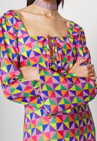 Barevné šaty vyrobené z hladké látky, s geometrickým vzorem trojúhelníků v růžové, zelené, modré a oranžové barvě. Hranatý výstřih a nabírané rukávy.