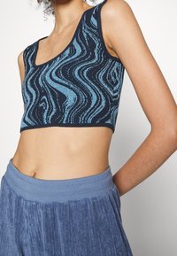 Námořnická modrá crop top s vlnitým vzorem v světlých modrých odst�ínech. Má kulatý výstřih a přiléhavý, žebrovaný spodní lem. Měkká textura.