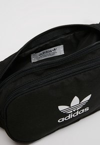 Black fabric pouch with a zip closure, featuring a white Adidas logo and label inside. Compact rectangular design with textured surface.