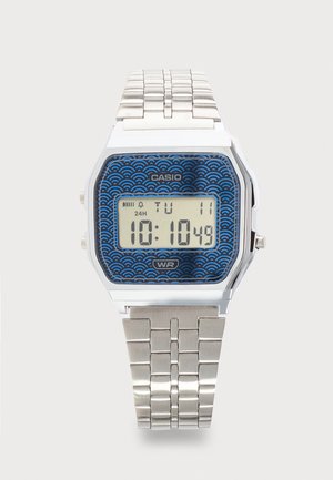 Digitális Casio karóra ezüst színű fém szíjjal, kék mintás számlappal, az idő 10:10:49-et mutat, nap kedd, dátum 11.