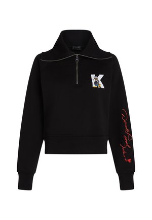 Svart cropped sweatshirt med høy krage, sølvglidelås og rød kursiv tekst på ermet. Har en tegneserielogo på forsiden.